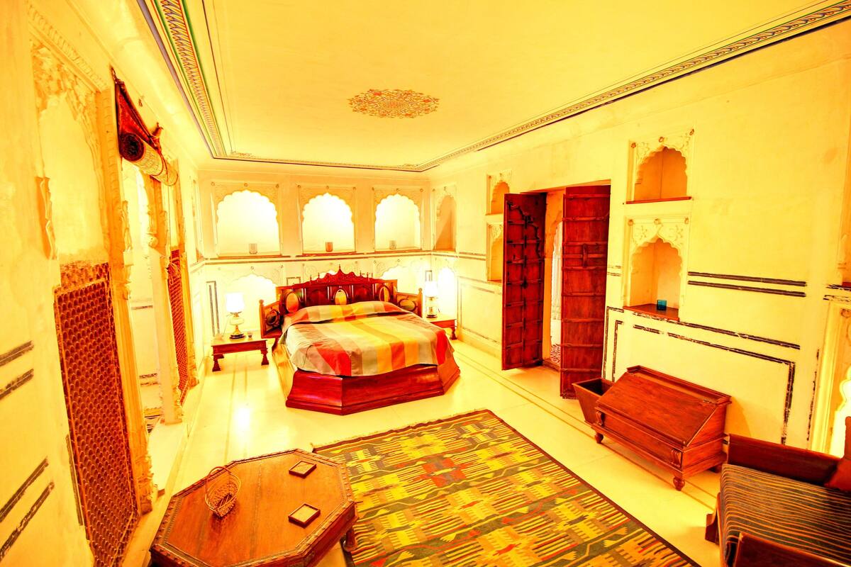 A traditional room with a large bed, a wooden chest, and a small table.