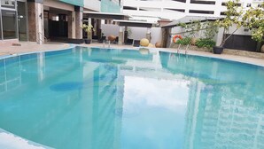 Una piscina con agua azul cristalina, rodeada por un porche cubierto con asientos y plantas en macetas.