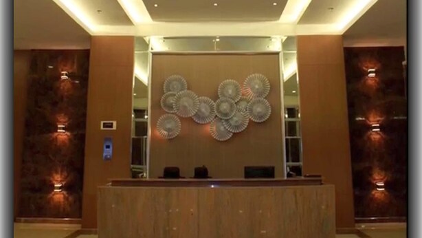 Un área de recepción moderna con una lámpara de araña central, un panel decorativo en la pared y un mostrador de recepción.