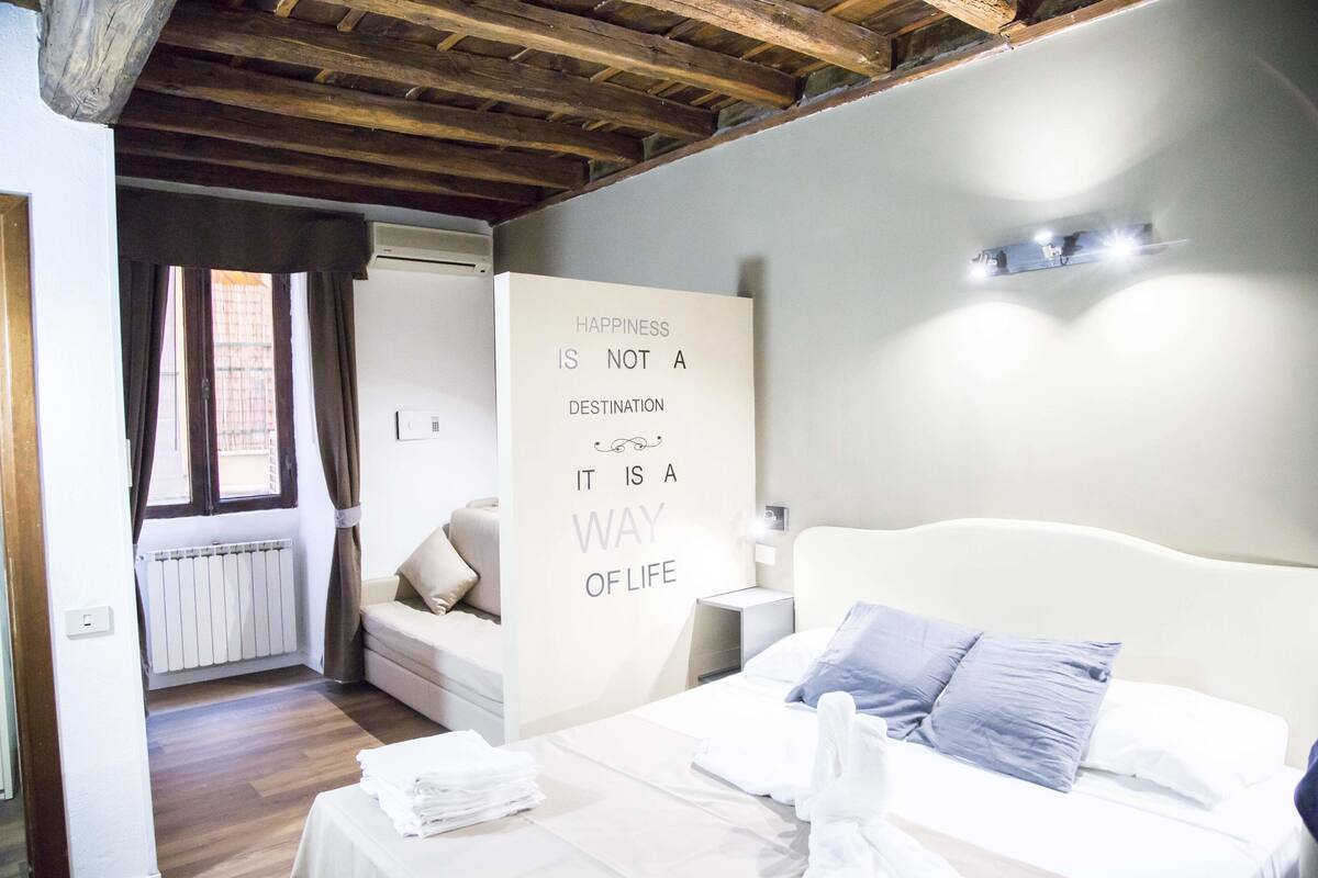 Une chambre à coucher avec un lit, une table de chevet, un mur orné d’une citation inspirante, une fenêtre avec des rideaux et un plafond en bois.