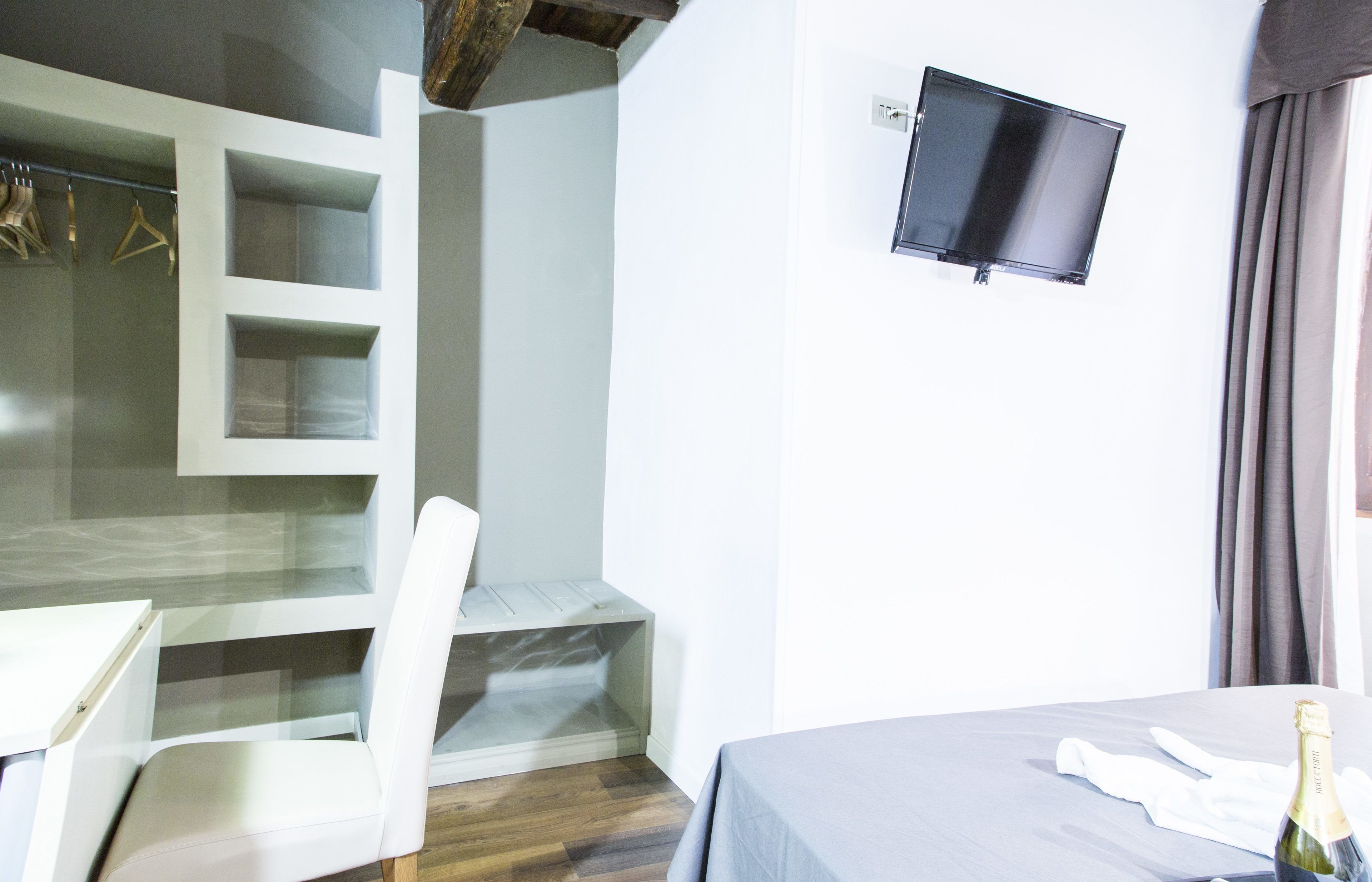 Ein Hotelzimmer mit Bett, Schreibtisch, Stuhl, einem an der Wand montierten Fernseher und einer Champagnerflasche.