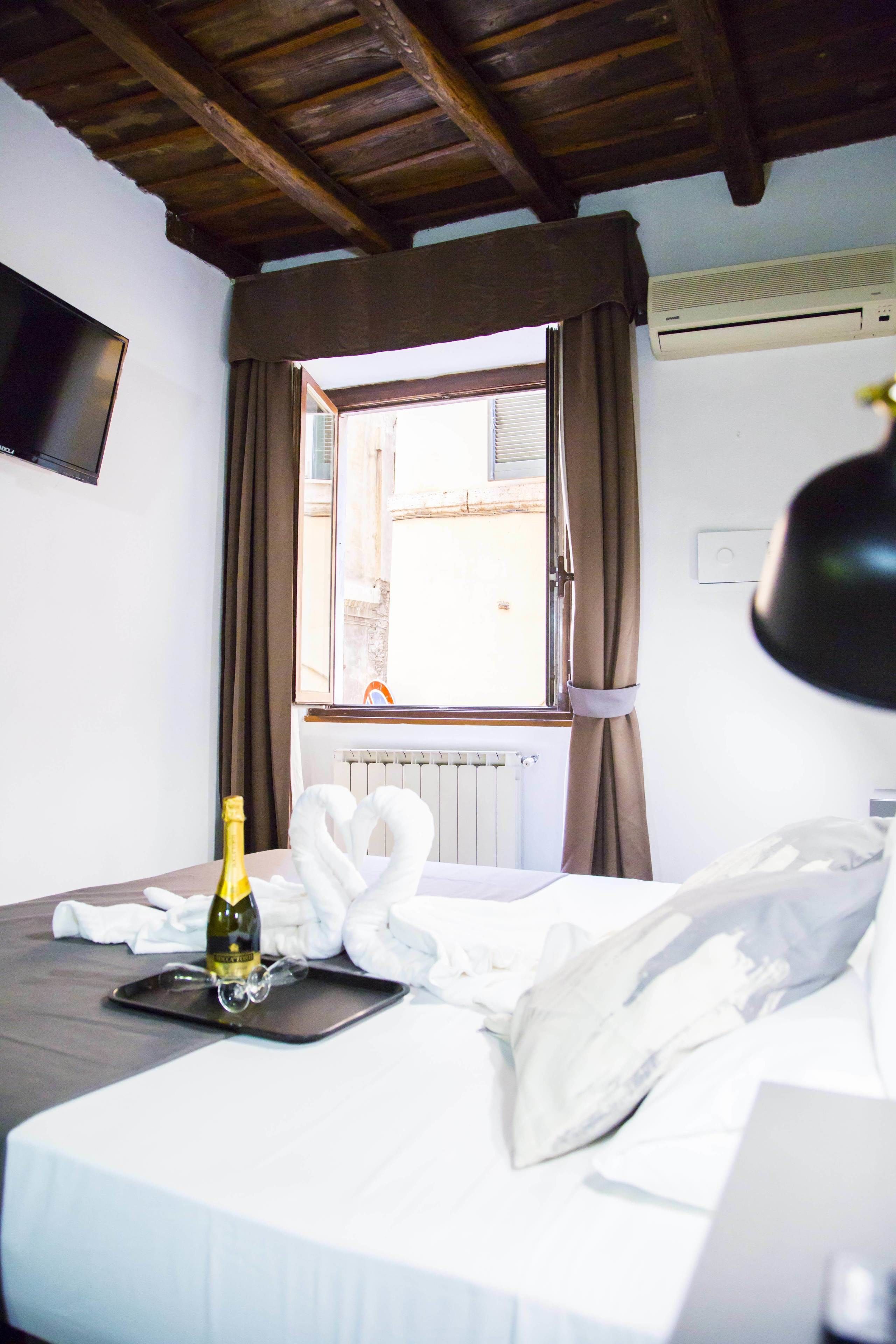 A hotel room with a bed, a bottle of champagne, a swan-shaped towel, and a window with curtains.