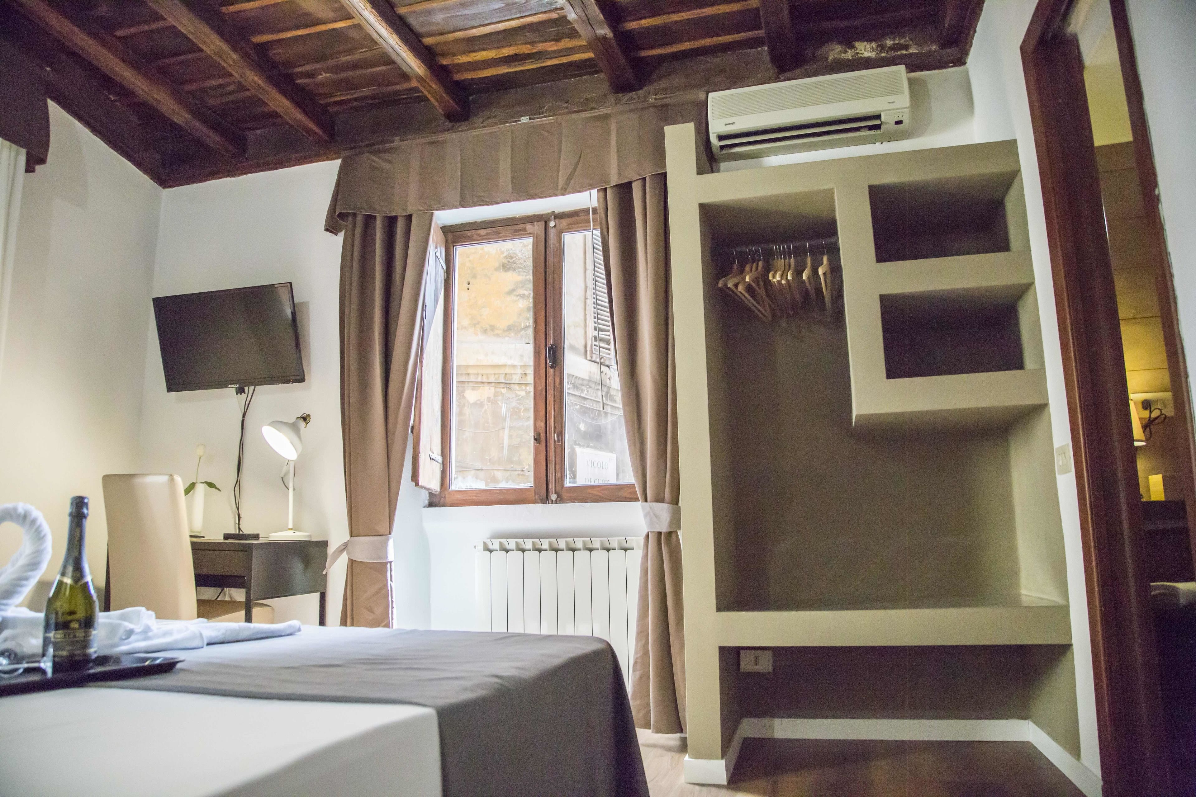A hotel room with a bed, a TV, a desk with a lamp, a window with curtains, and a wardrobe.