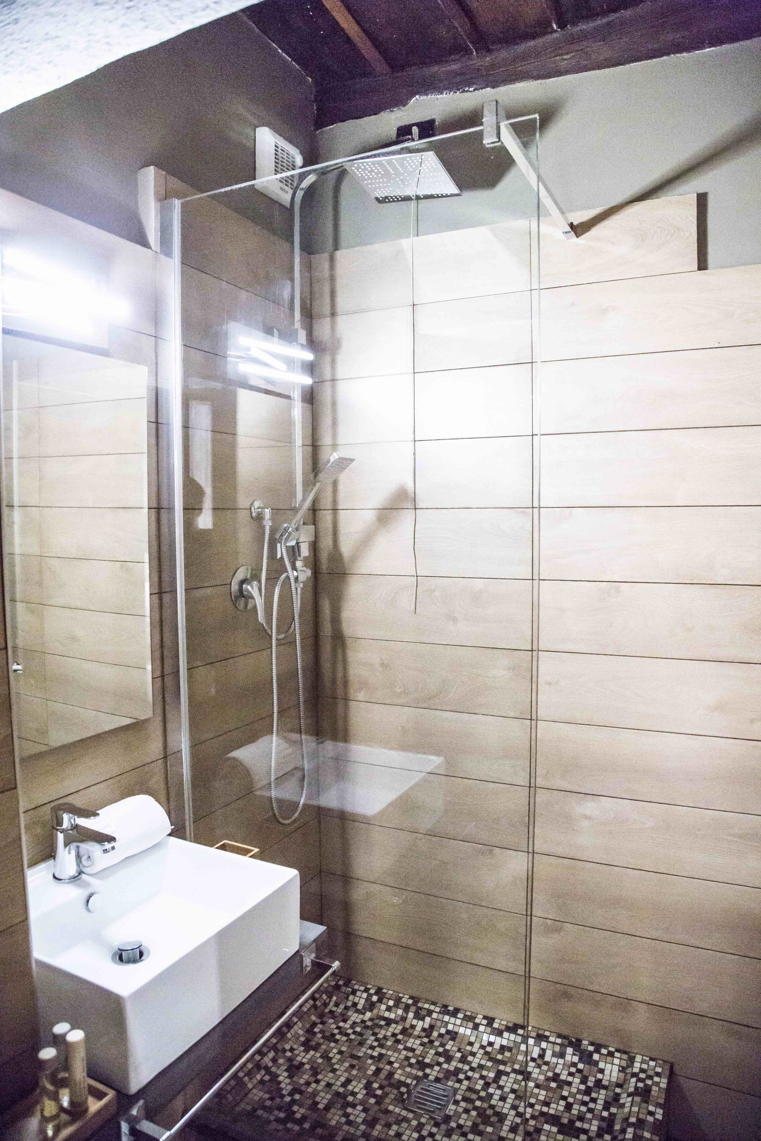 A modern bathroom with a glass-enclosed shower, a white sink, and a tiled floor.