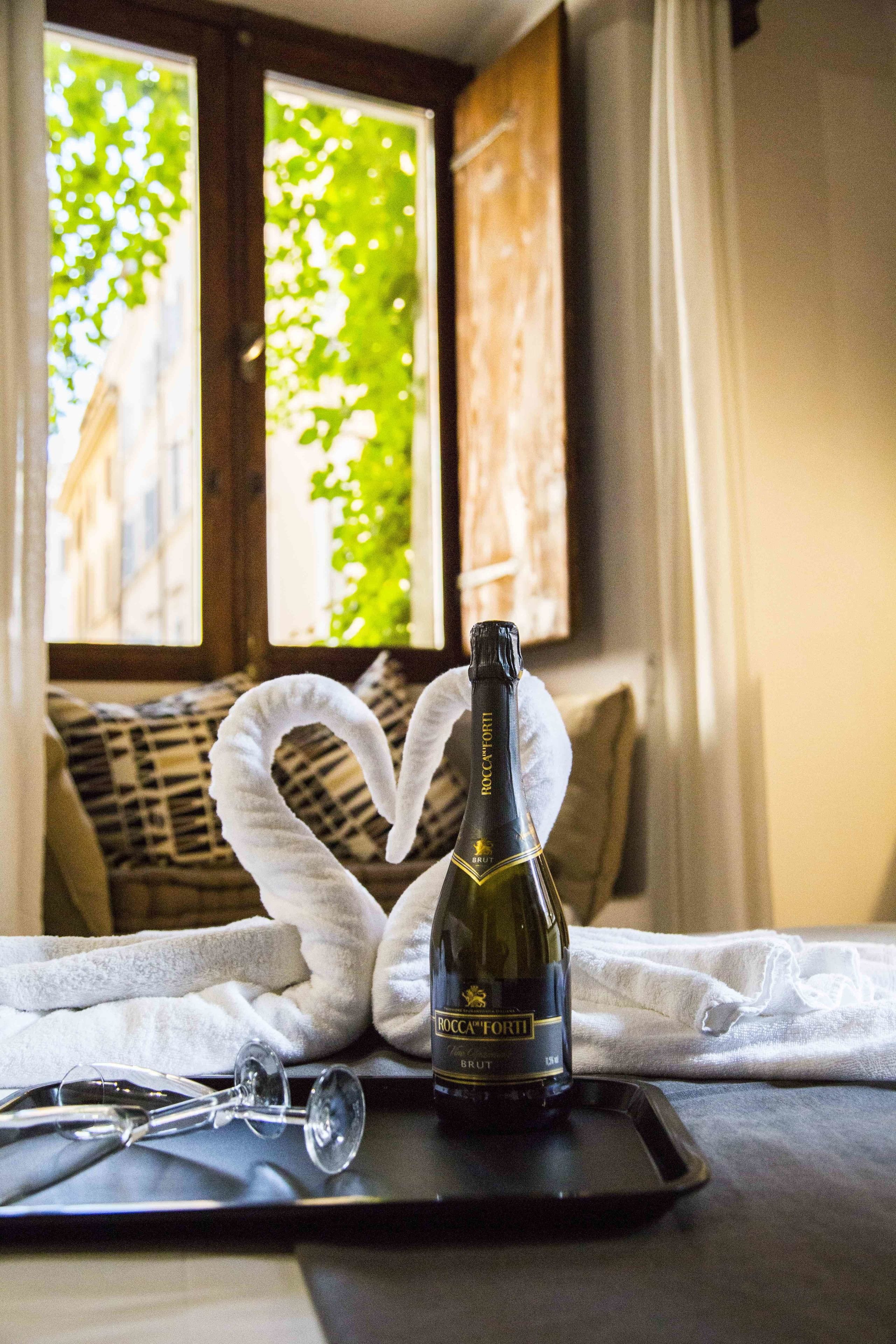Una botella de vino sobre una bandeja con una toalla con forma de corazón en una cama.
