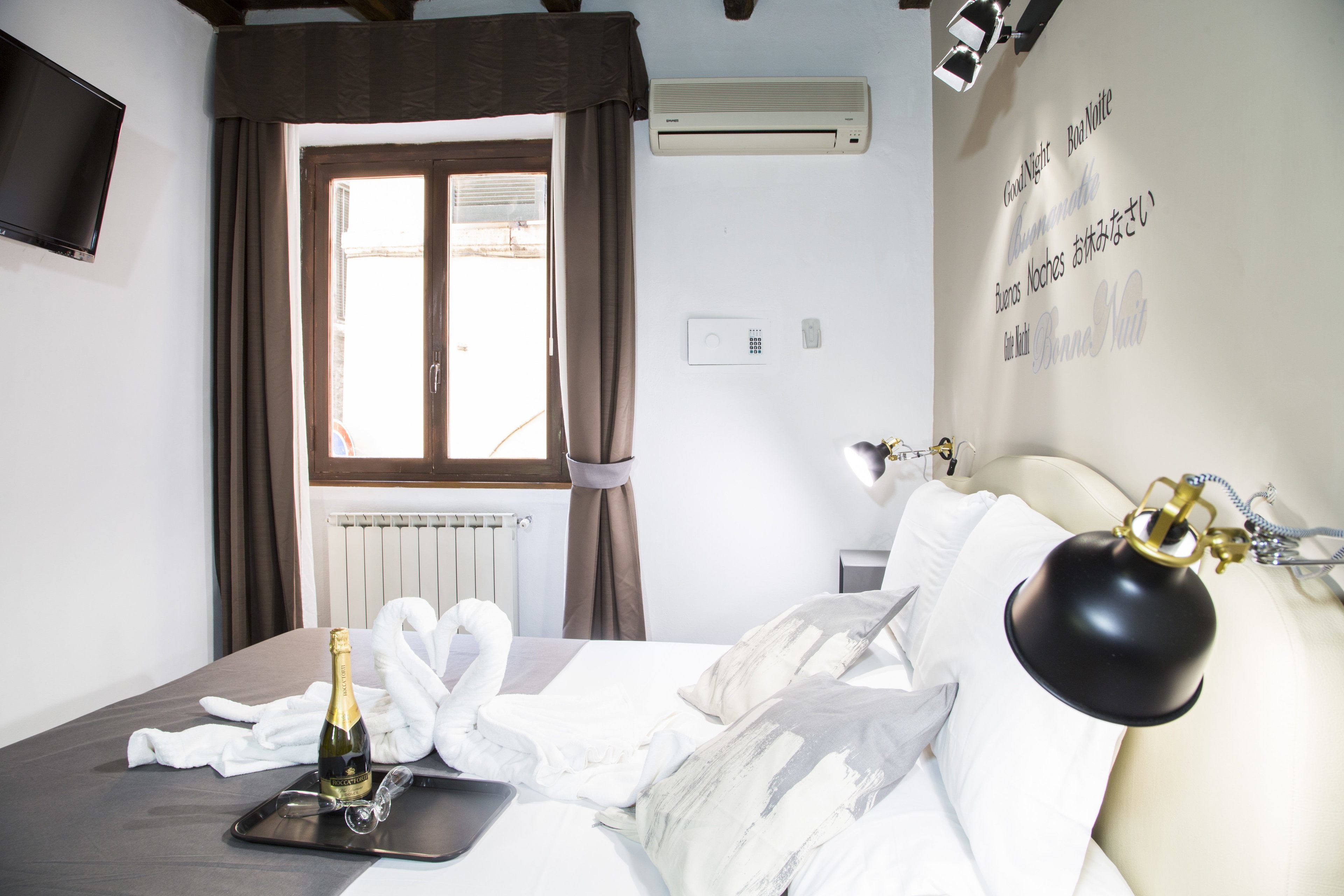 A hotel room with a bed, a bottle of champagne, a swan-shaped towel, and a wall-mounted air conditioner.