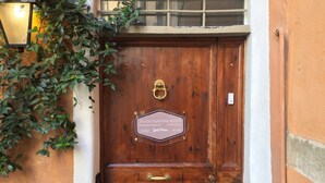 Eine hölzerne Doppeltür mit einer Schrifttafel, ein kleiner Podeststufenaufgang davor und eine Wandleuchte links.