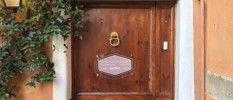 A wooden double door with a plaque, a small step leading up to it, and a wall-mounted light fixture to the left.