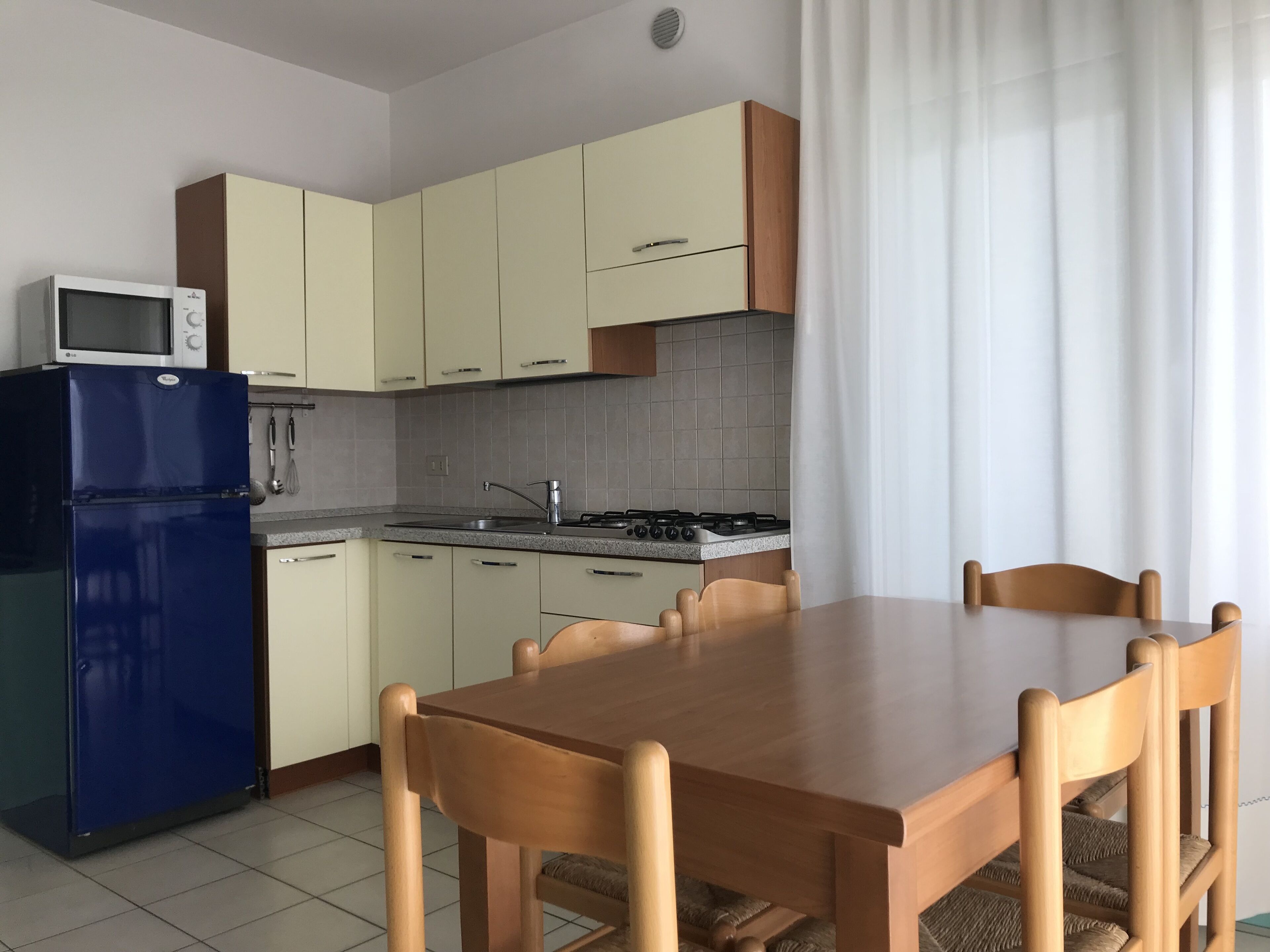Une cuisine moderne avec des meubles de couleur claire, un réfrigérateur bleu, une cuisinière à gaz et une table à manger en bois avec des chaises.