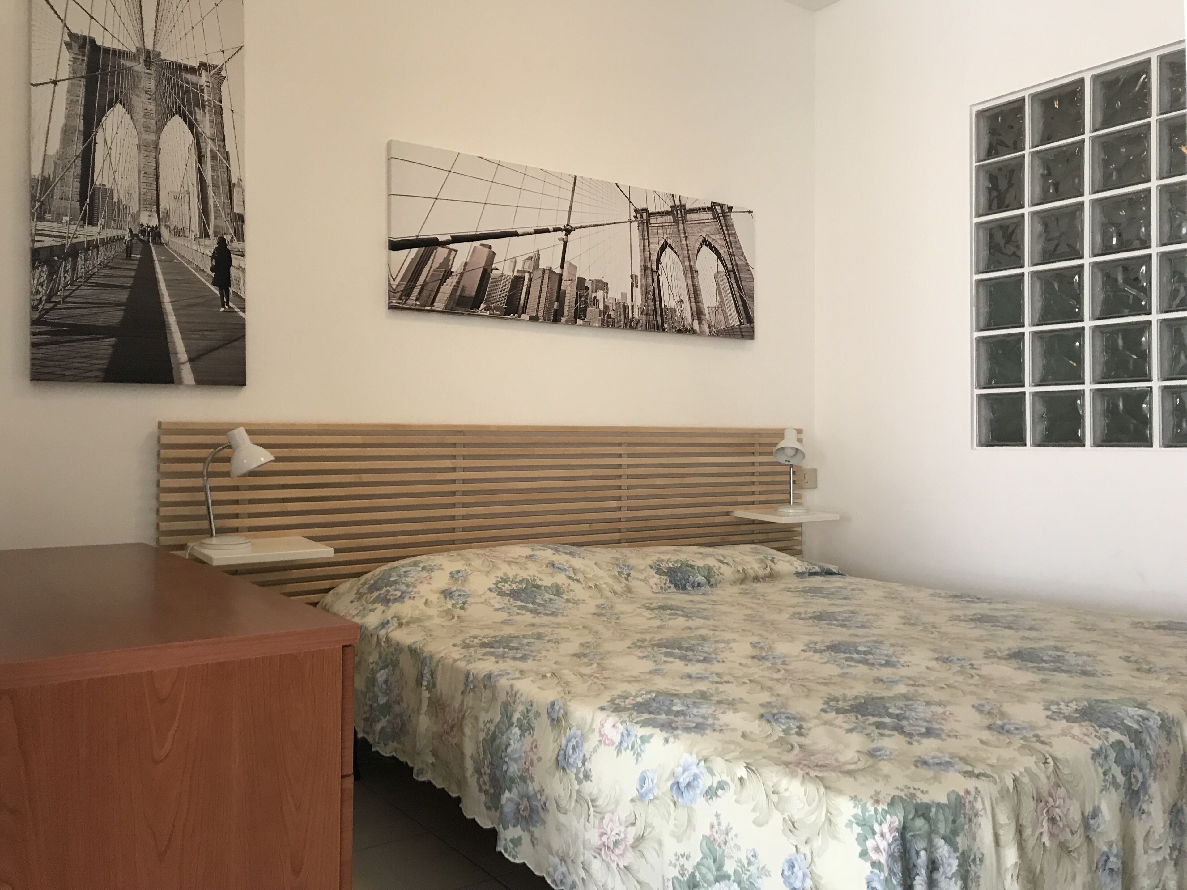 Una camera da letto con una testiera in legno, una copriletto floreale, una scrivania e due lampade a parete.