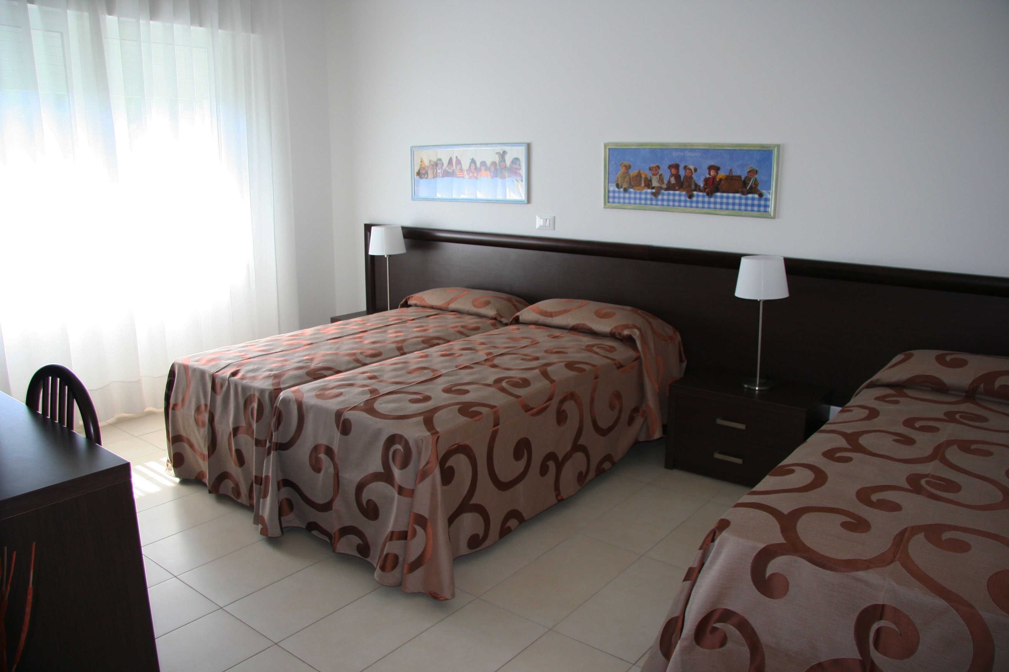 Habitación de hotel con dos camas, un escritorio y una silla. Hay dos lámparas de pared y dos cuadros colgados en la pared.