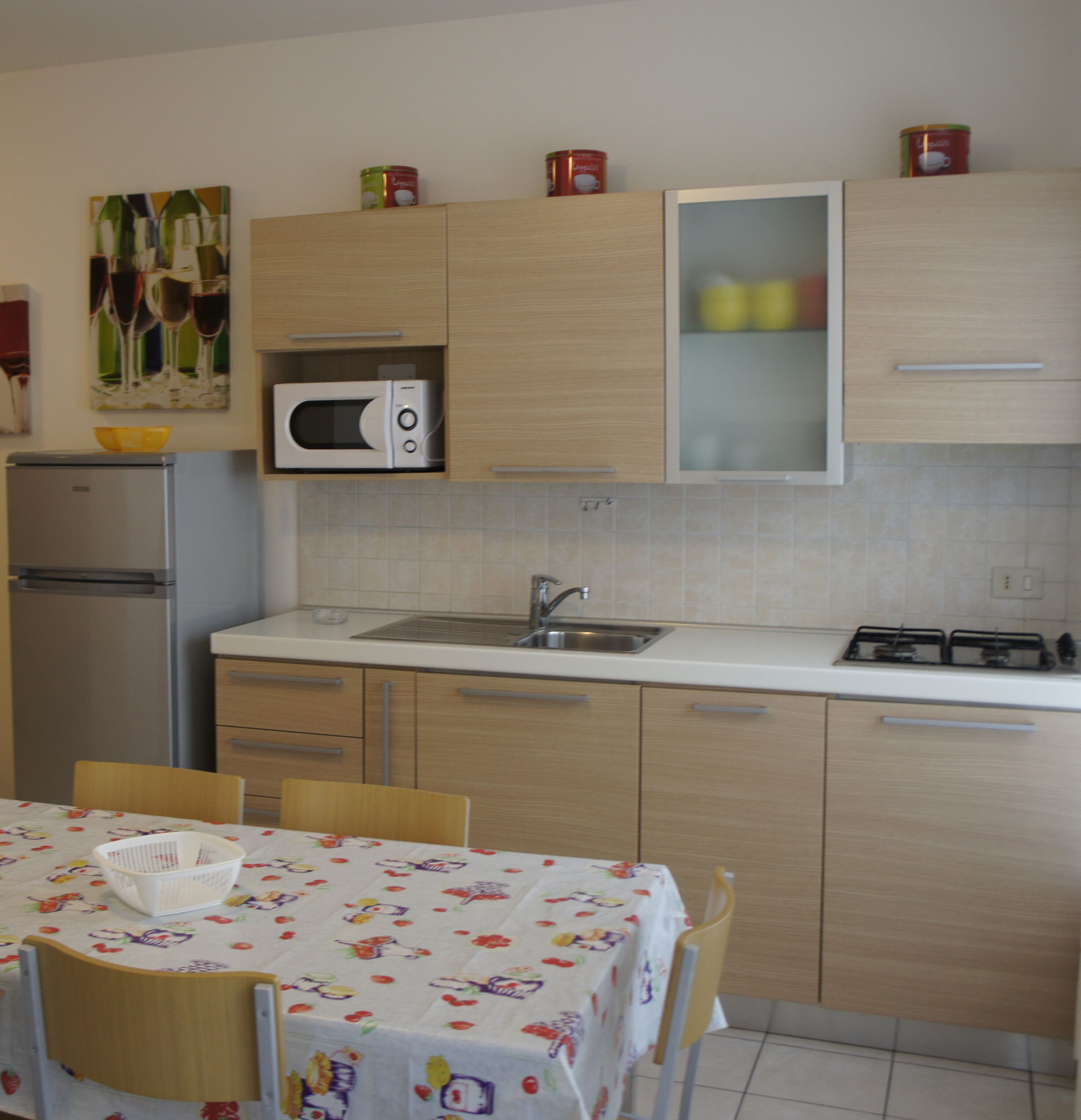 A compact kitchen with a microwave, sink, and stove. There is a dining table with chairs and a fruit basket.