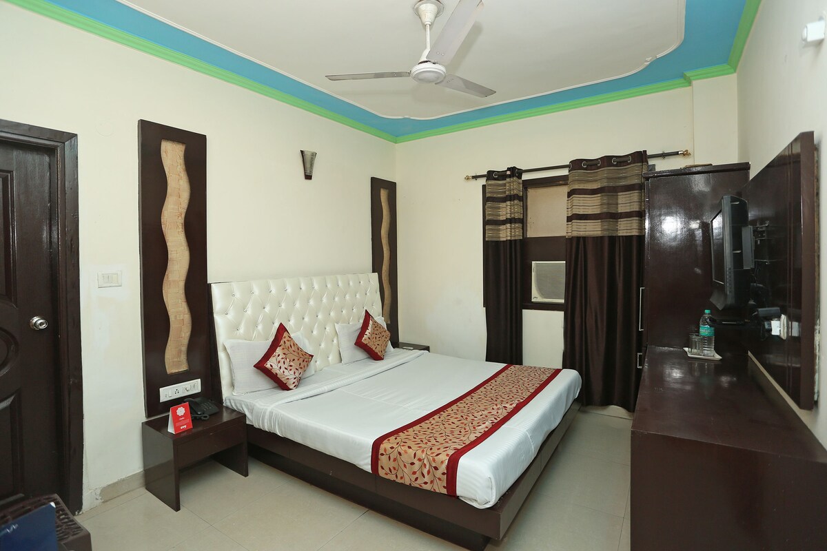 A bedroom with a bed, a nightstand, a desk, a ceiling fan, and a window with curtains.