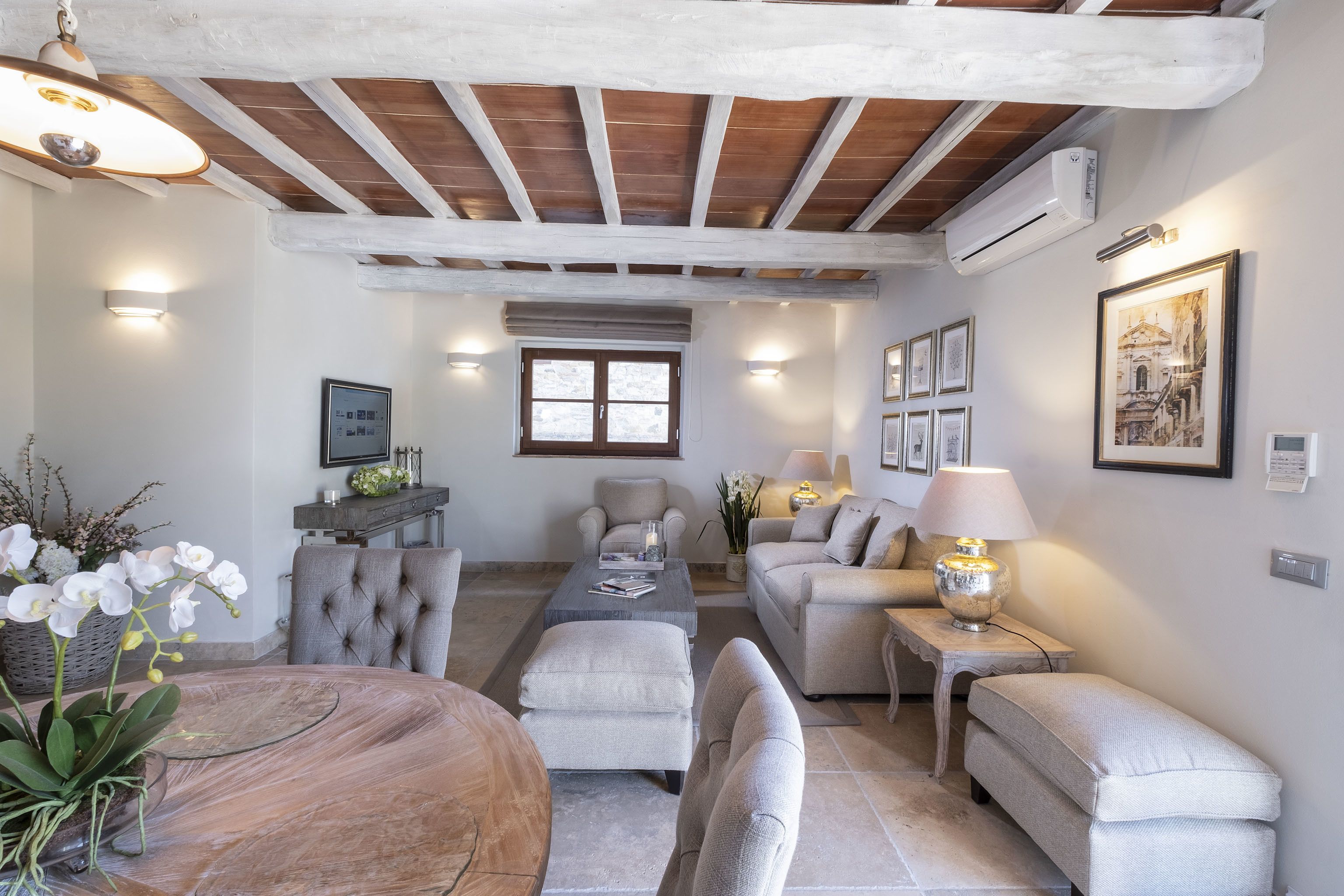 Un salón amplio con techo de madera, una mesa de comedor redonda y un área de estar cómoda con sofá y sillones.
