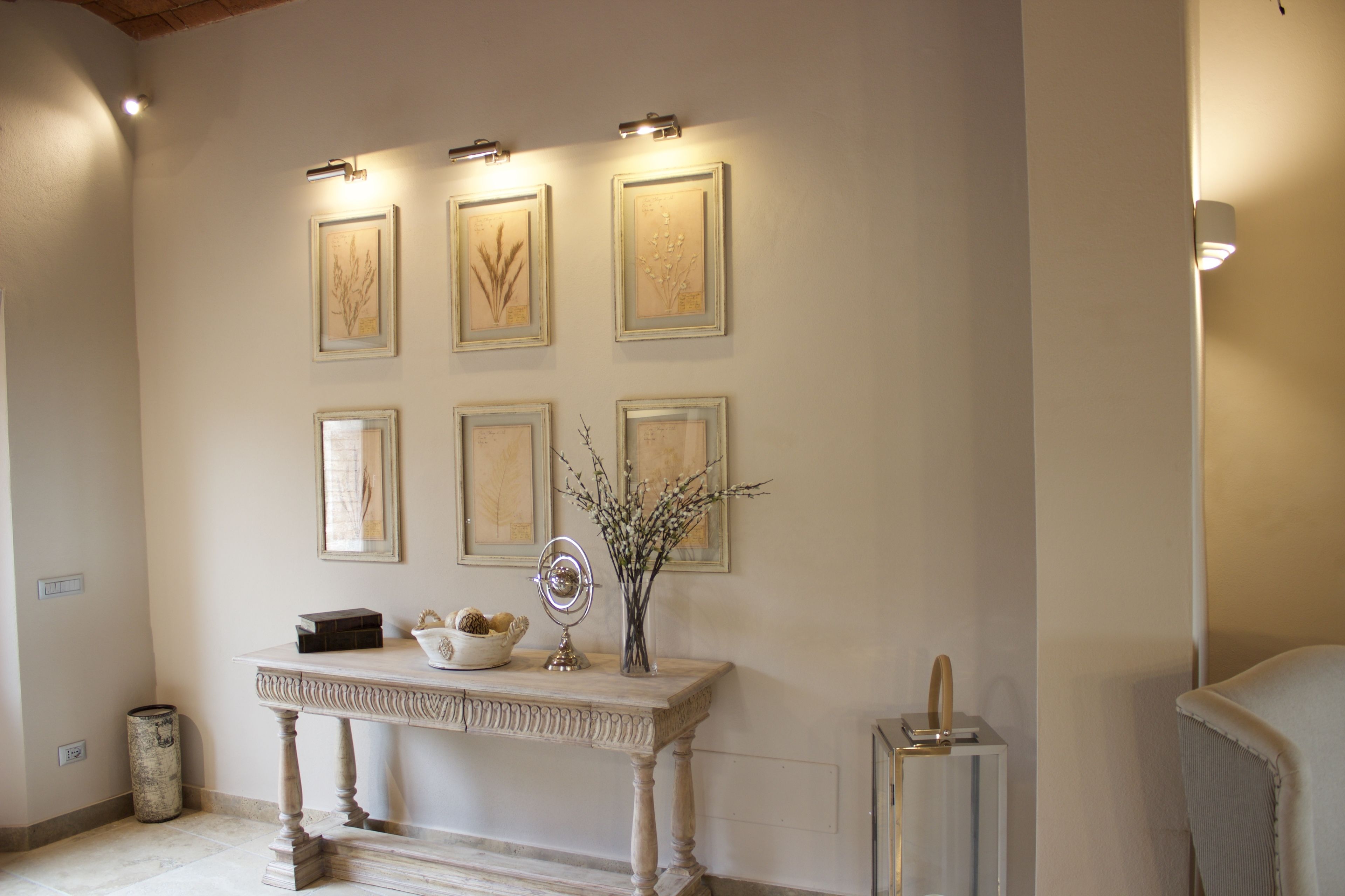 A hallway with framed botanical prints on the wall, a console table with decorative items, and a small mirror.