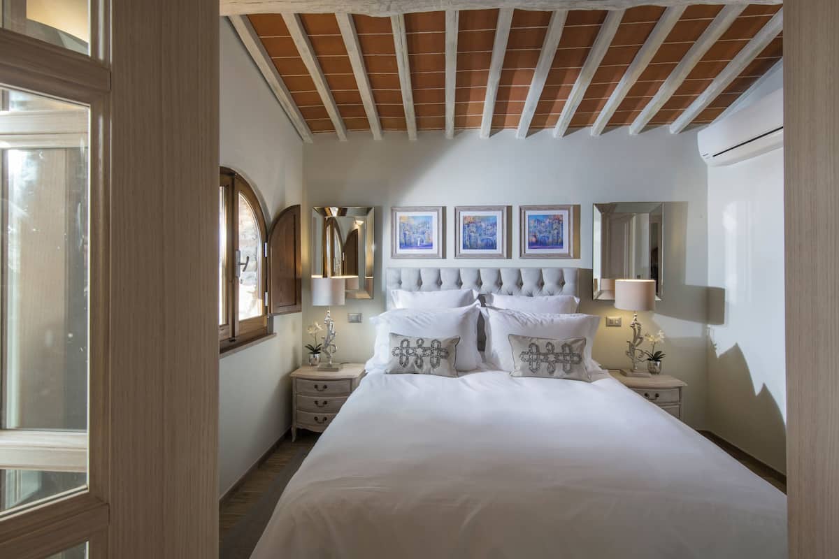 Une chambre à coucher avec un grand lit, deux tables de chevet, un miroir et des œuvres d’art encadrées accrochées au mur.