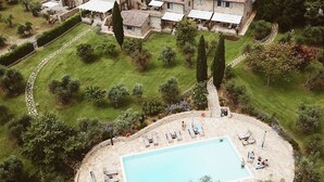 A villa with a swimming pool surrounded by a garden, set in a rural landscape with vineyards in the background.