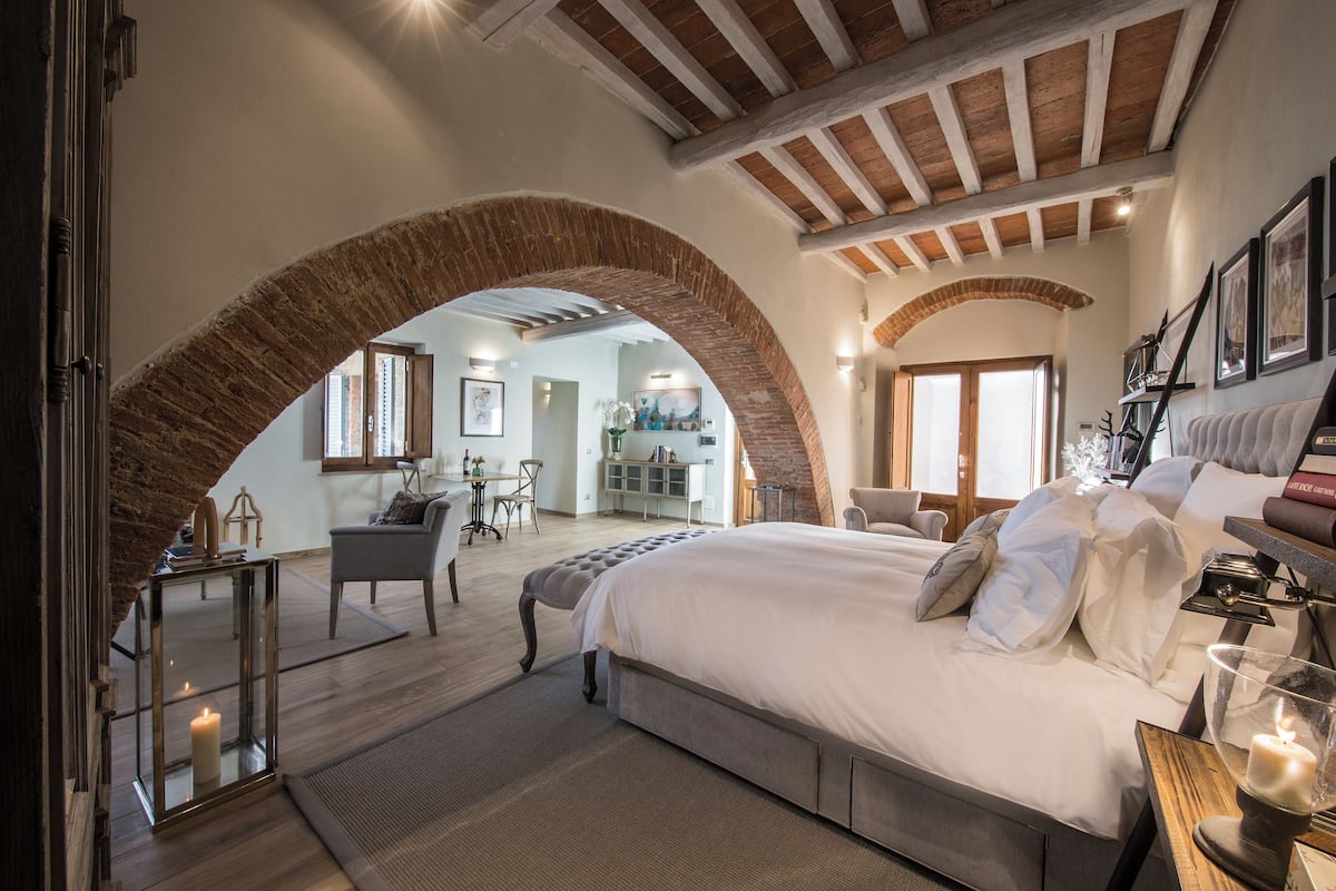 Une chambre avec un grand lit, un plafond en bois et une arche en briques.