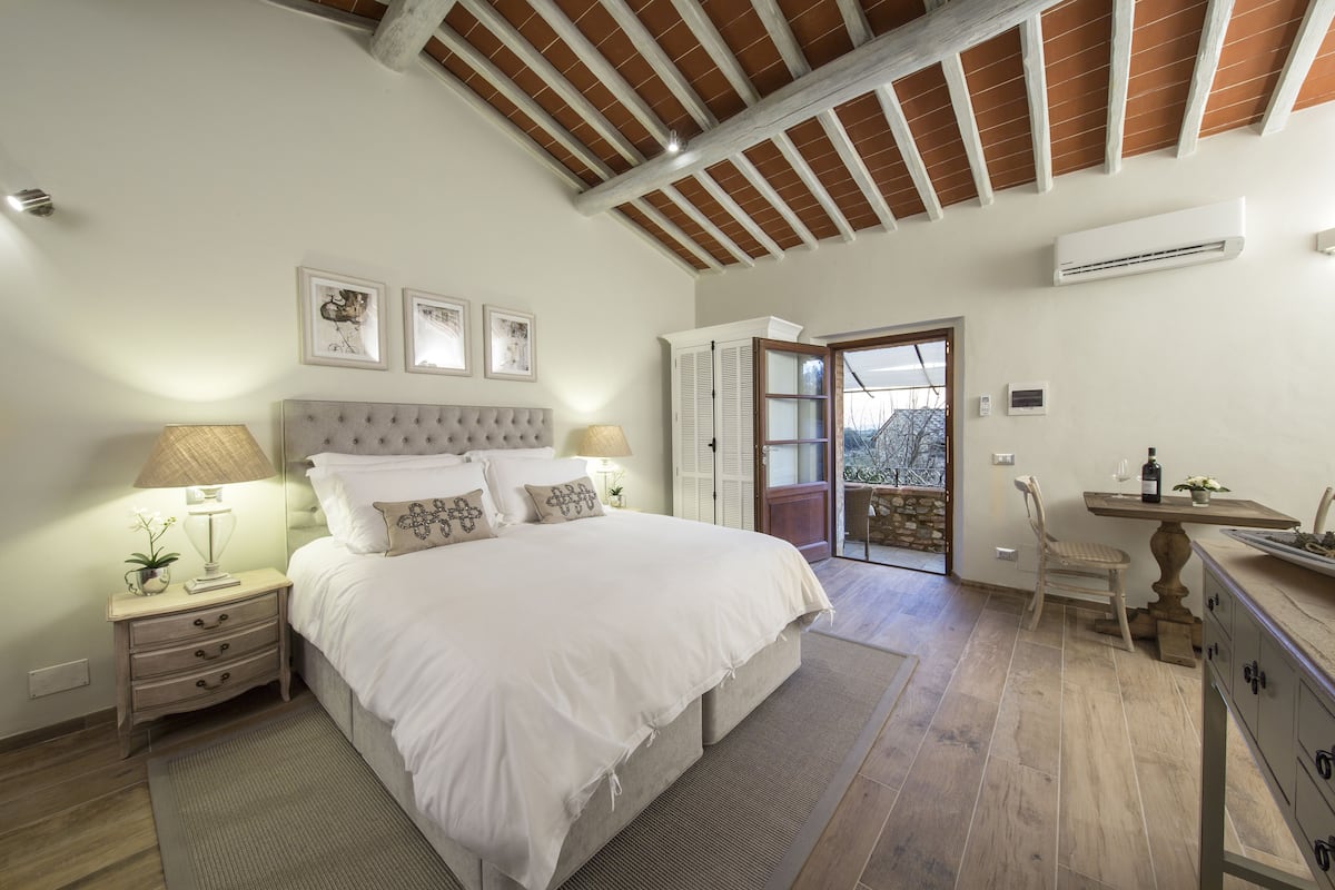 Une chambre avec un grand lit, des lampes de chevet, une table de nuit, une commode et une porte-fenêtre donnant sur un balcon.