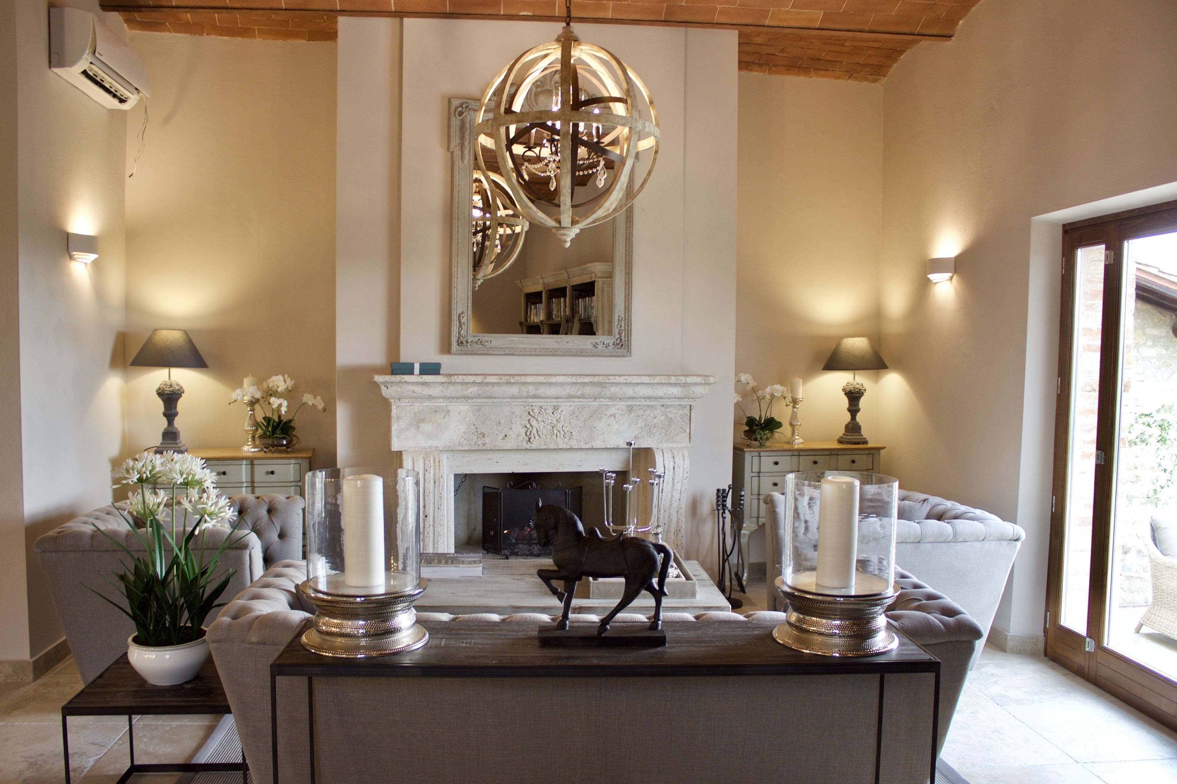 A living room with a fireplace, two sofas, a coffee table with decorative items, and a chandelier.
