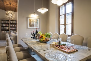 A dining area with a long table set for six, surrounded by chairs, with a bookshelf and a painting on the wall.