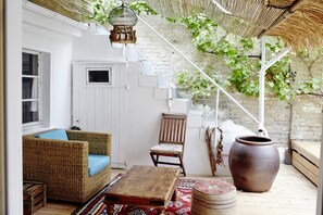 Un espace extérieur accueillant, aménagé avec des meubles en osier, une table en bois et un grand pot en terre cuite.
