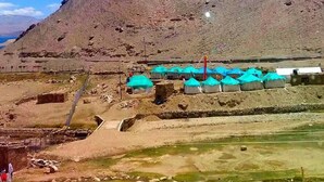 Paisaje montañoso con varias yurtas y un pequeño edificio, presumiblemente una posada o albergue, en un entorno árido y pedregoso.