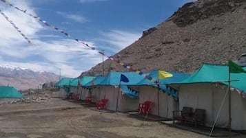 A row of tents with prayer flags, set against a mountainous backdrop.