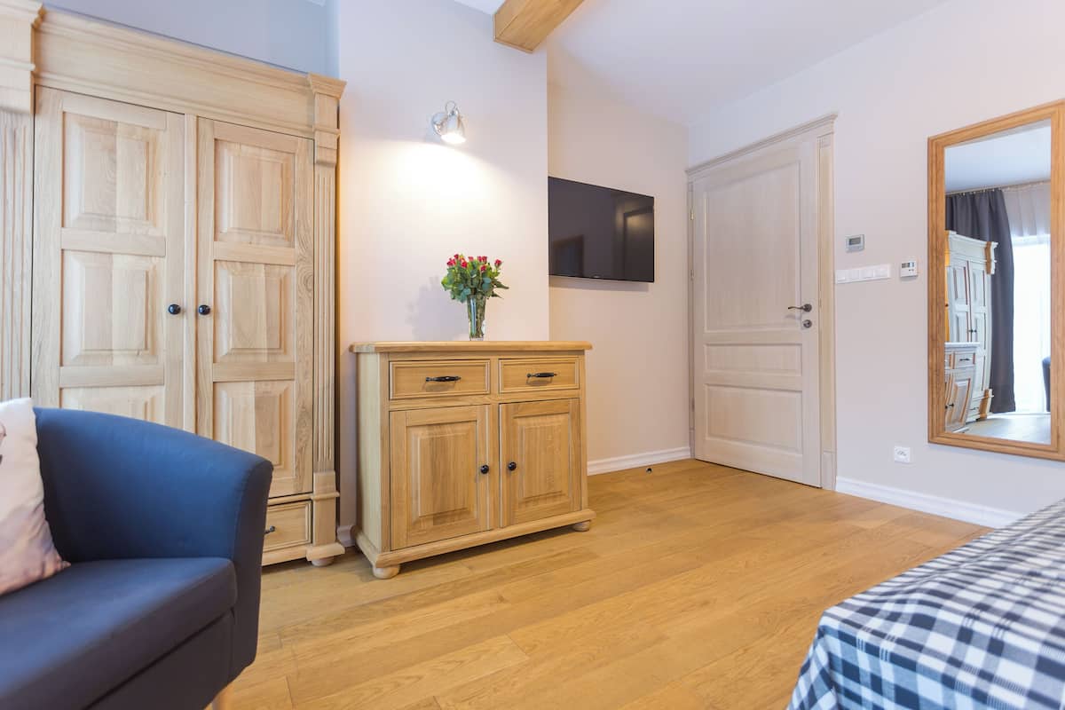 A room with wooden flooring, a blue sofa, a wooden cabinet with drawers, a flat-screen TV, and a mirror on the wall.