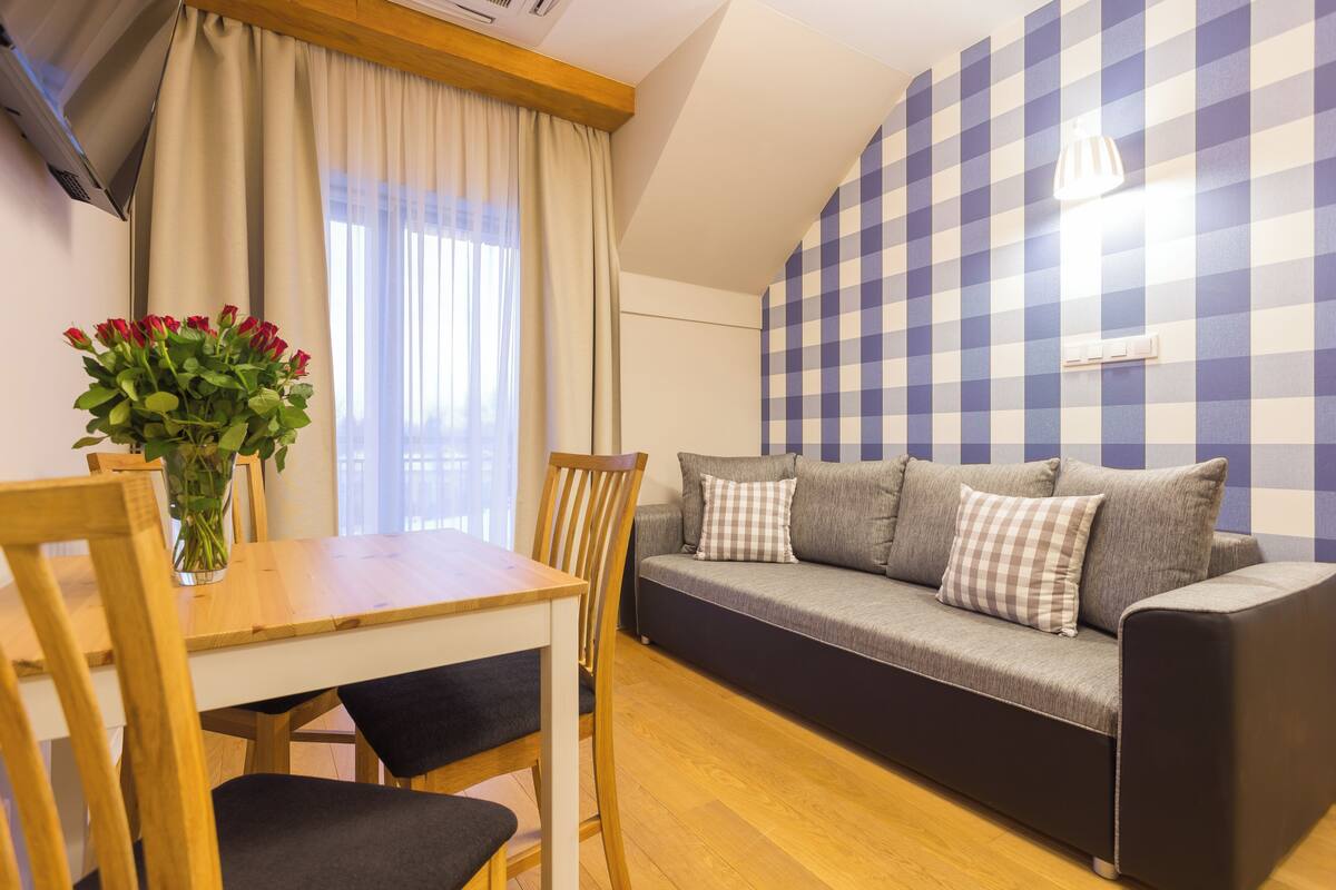 A living room with a sofa, a dining table with chairs, and a vase of flowers.