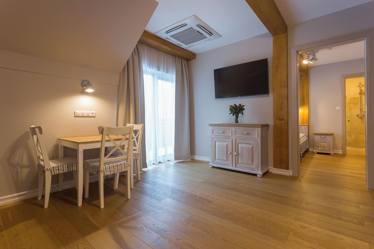 A spacious room with a wooden floor, a dining table with chairs, a white cabinet, and a mounted TV.