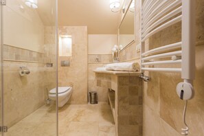 A modern bathroom with a glass shower enclosure, a toilet, a sink with a towel rack, and a mirror.