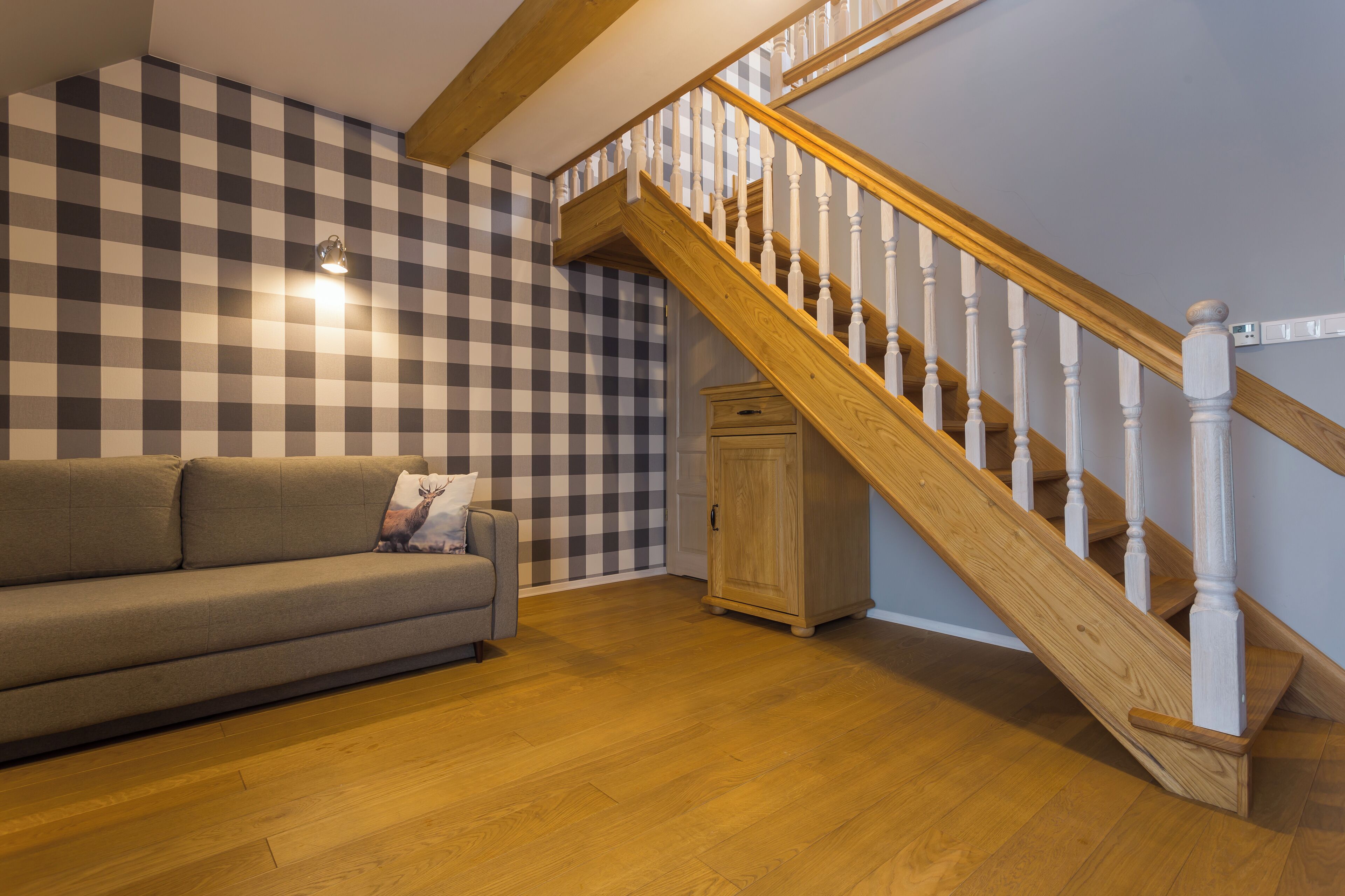 A living room with a wooden staircase, a checkered wall, and a sofa.