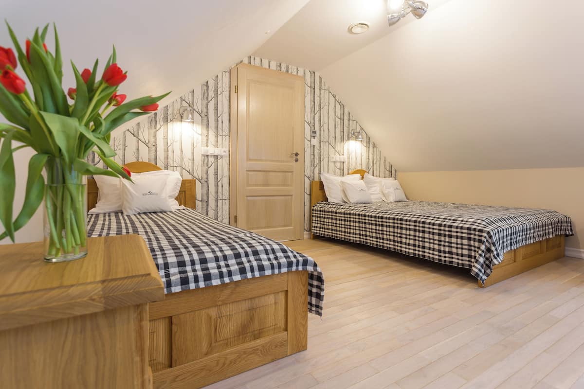 A bedroom with two beds, a wooden dresser, a vase with red flowers, and a door with a patterned wallpaper.