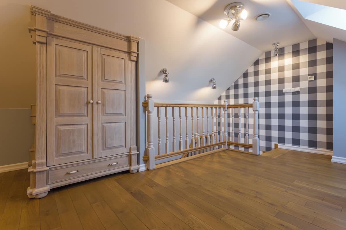 A spacious room with a wooden floor, a large wardrobe, a staircase with a railing, and a checkered wall.