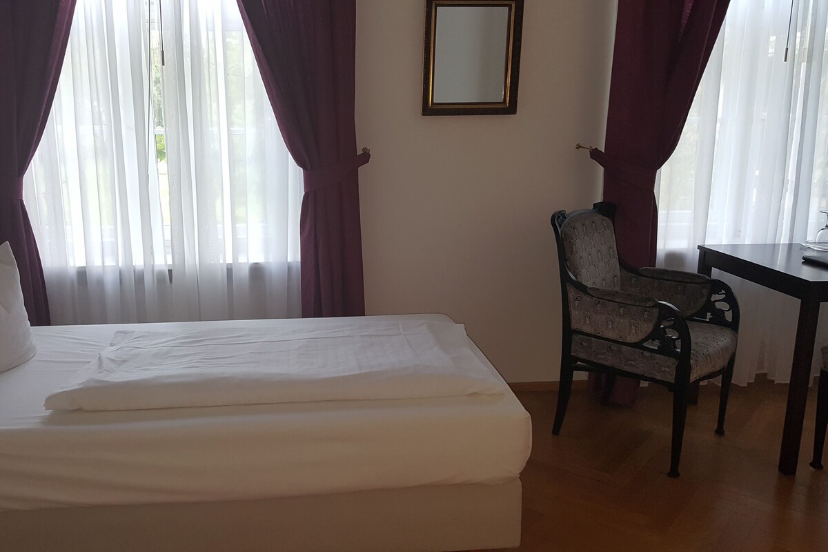 Ein Hotelzimmer mit Bett, Stuhl, Tisch und einem Spiegel an der Wand.