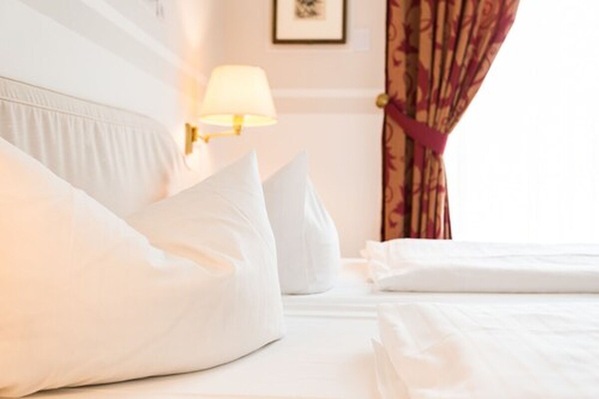 Ein Hotelzimmer mit ordentlich bezogenen Betten, einer Lampe auf dem Nachttisch und einer Tür mit Vorhang.