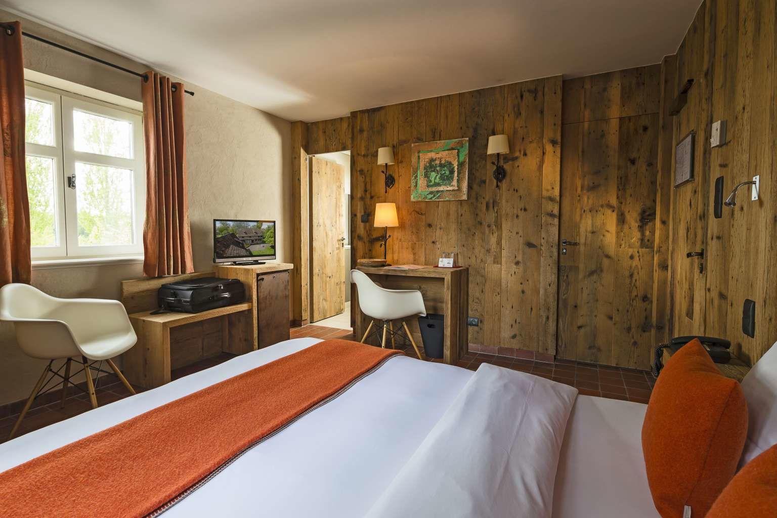 Una habitación de hotel con cama, escritorio, silla, televisor y paredes de madera.