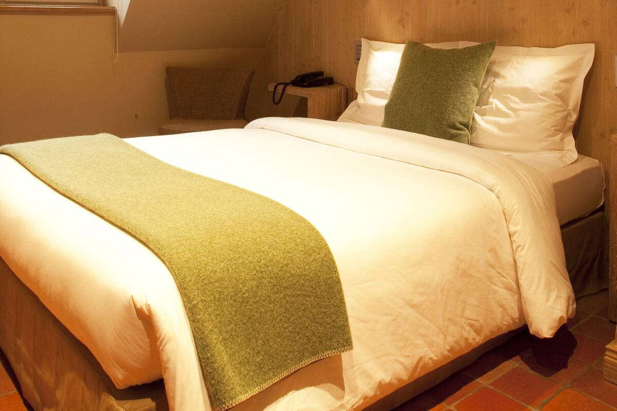 Een slaapkamer met een bed, een nachtkastje, een lamp en een raam met uitzicht.