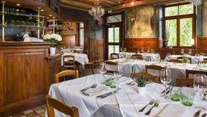 Un restaurante con interiores de madera, manteles blancos y copas de vidrio verde.