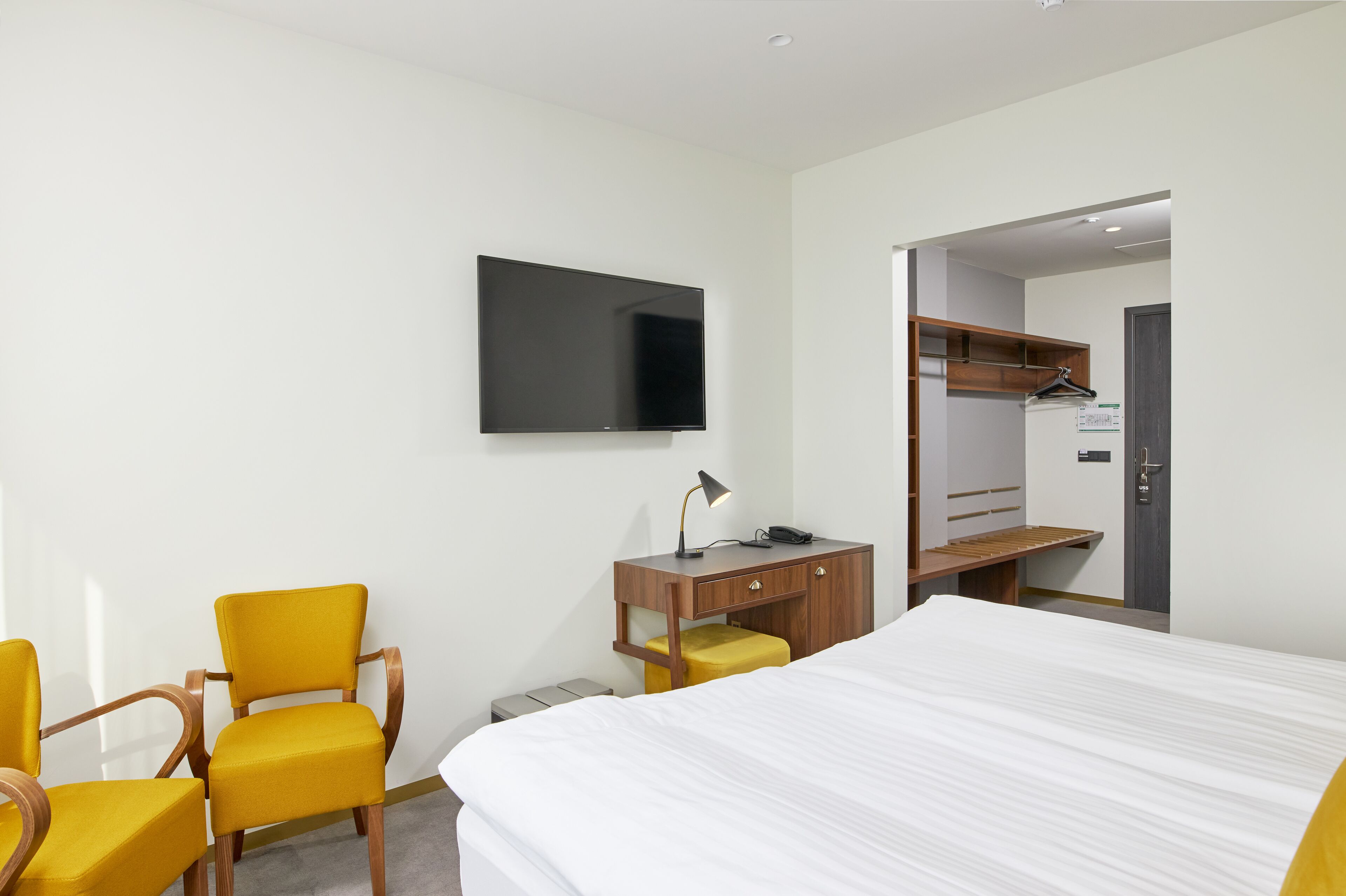 Une chambre d’hôtel comprenant un lit, un bureau avec une chaise, une télévision et une armoire.