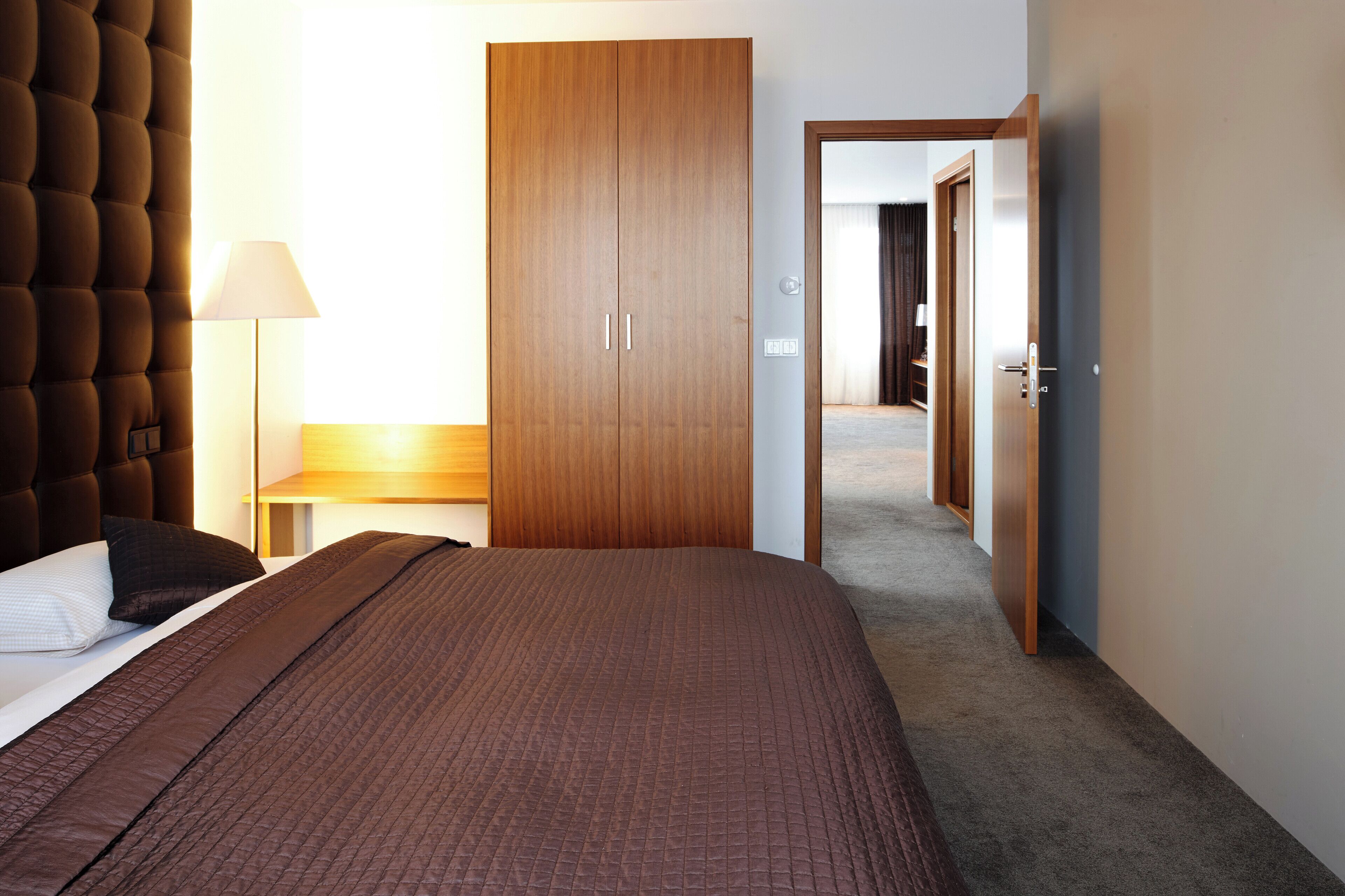 Een hotelkamer met een groot bed, een garderobe, een nachtkastje met een lamp en uitzicht op de gang.