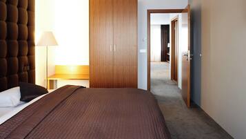 Een hotelkamer met een groot bed, een garderobe, een nachtkastje met een lamp en uitzicht op de gang.