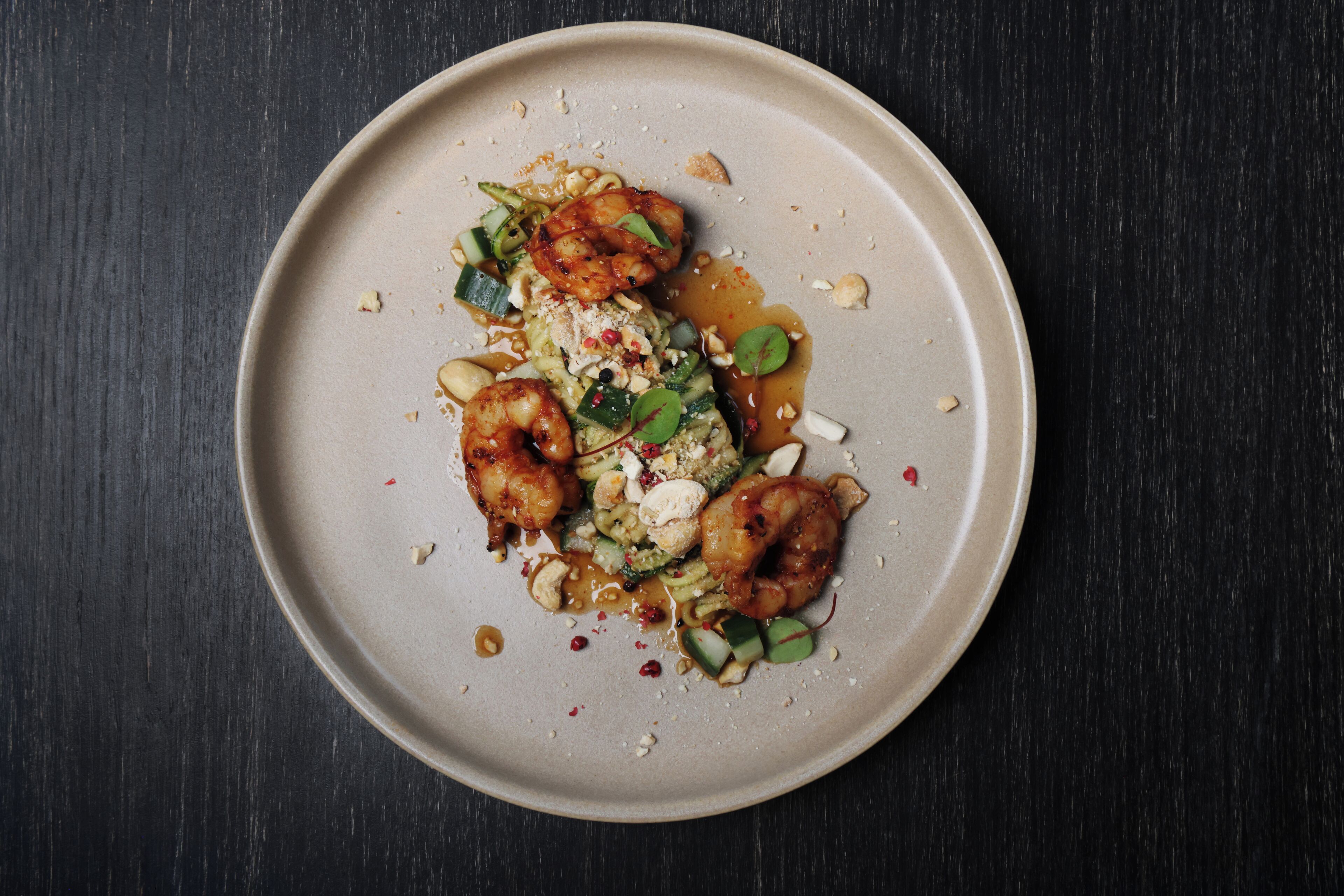 A plate of food with shrimp, vegetables, and sauce on a dark surface.