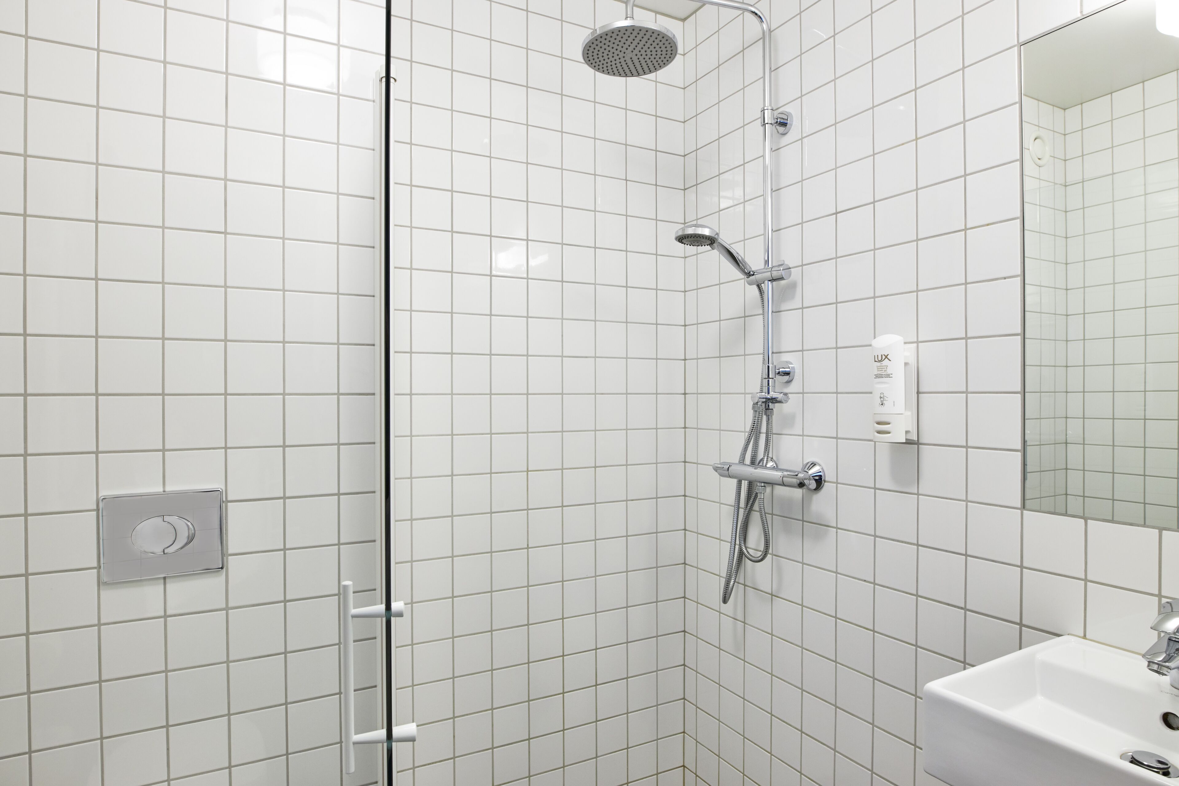 A modern bathroom with white tiled walls, a glass shower enclosure, a white sink, and a mirror.