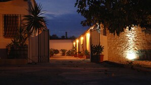 A building with a gated entrance, potted plants, and a stone wall with lights. - A Lumìa (Noto)