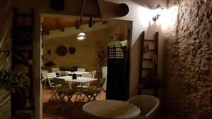 A rustic dining area with a wooden table and chairs, a hanging light fixture, and a stone wall. - A Lumìa (Noto)