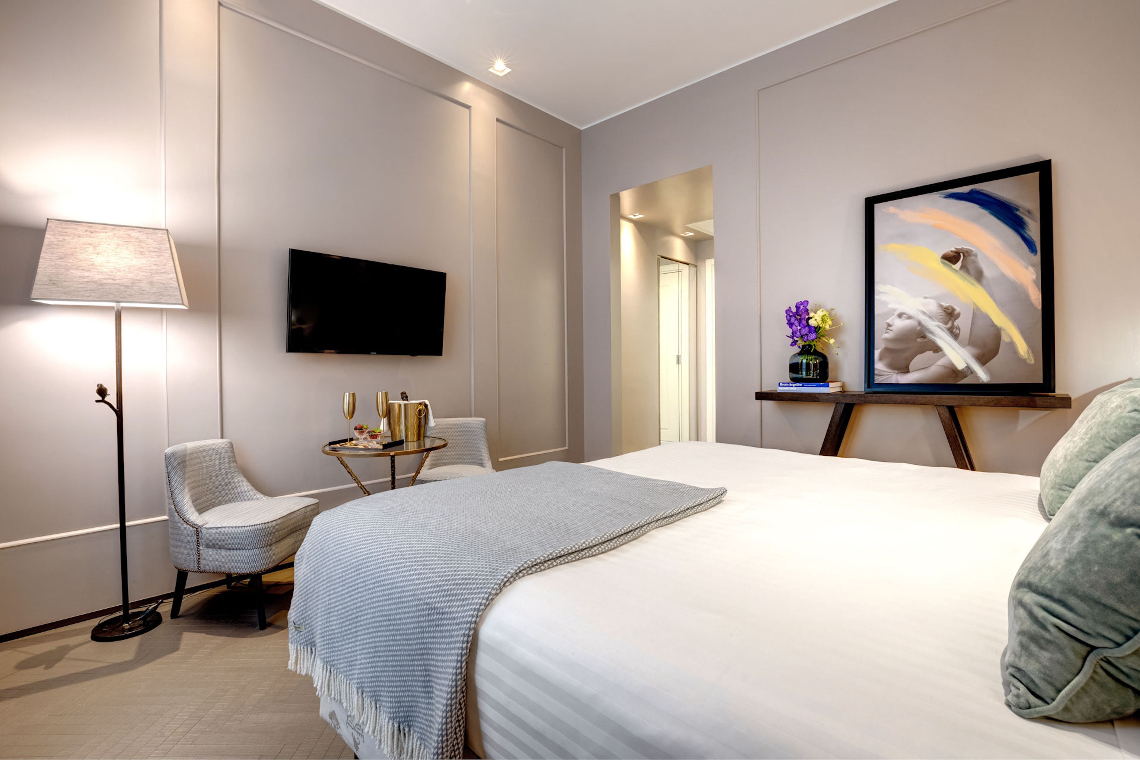 Una habitación de hotel moderna con una cama grande, un televisor de pantalla plana, un escritorio con lámpara y un cuadro en la pared.