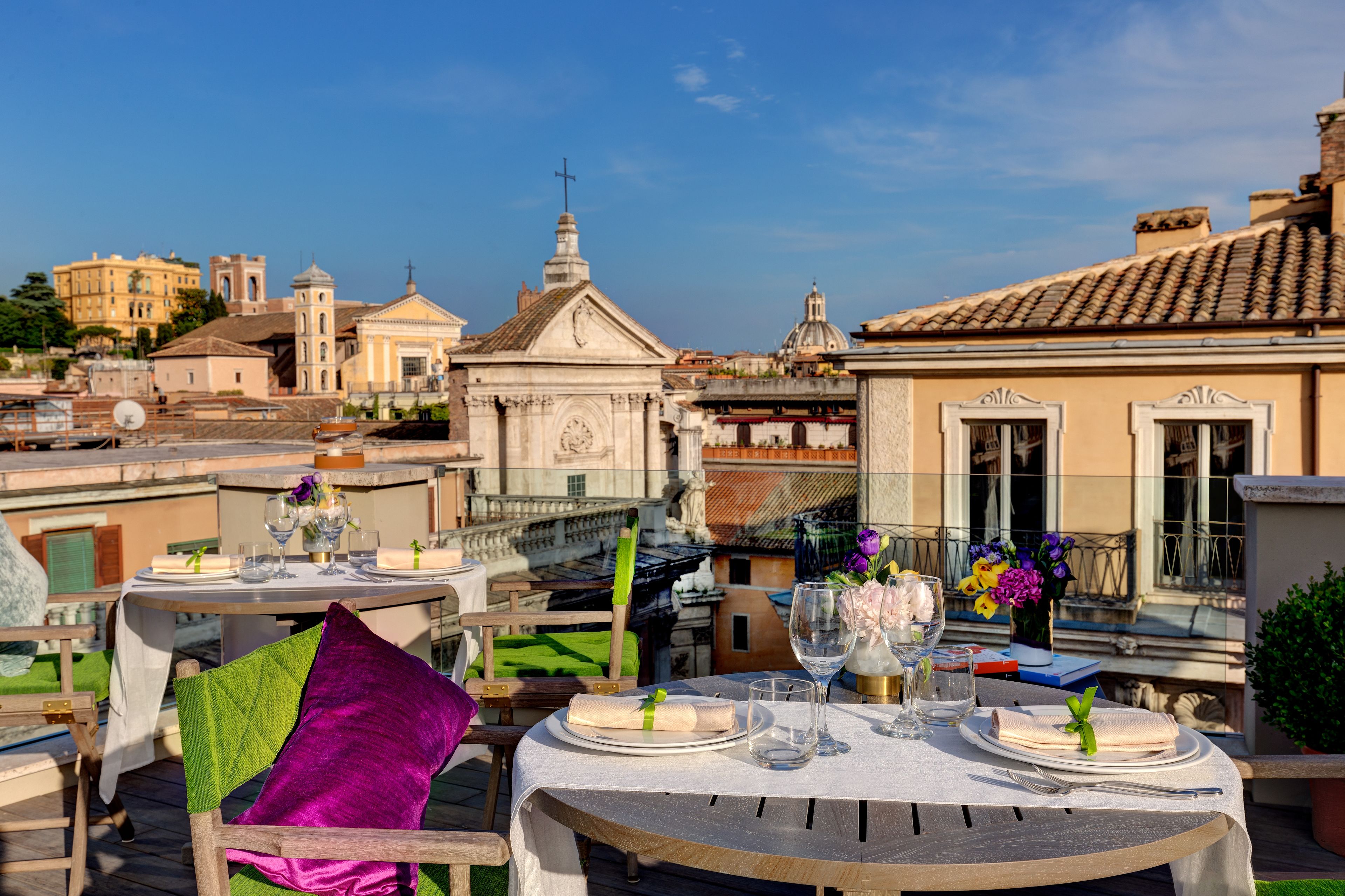 Une terrasse sur le toit, avec des tables dressées pour le dîner, offrant une vue sur des bâtiments historiques et un ciel dégagé.