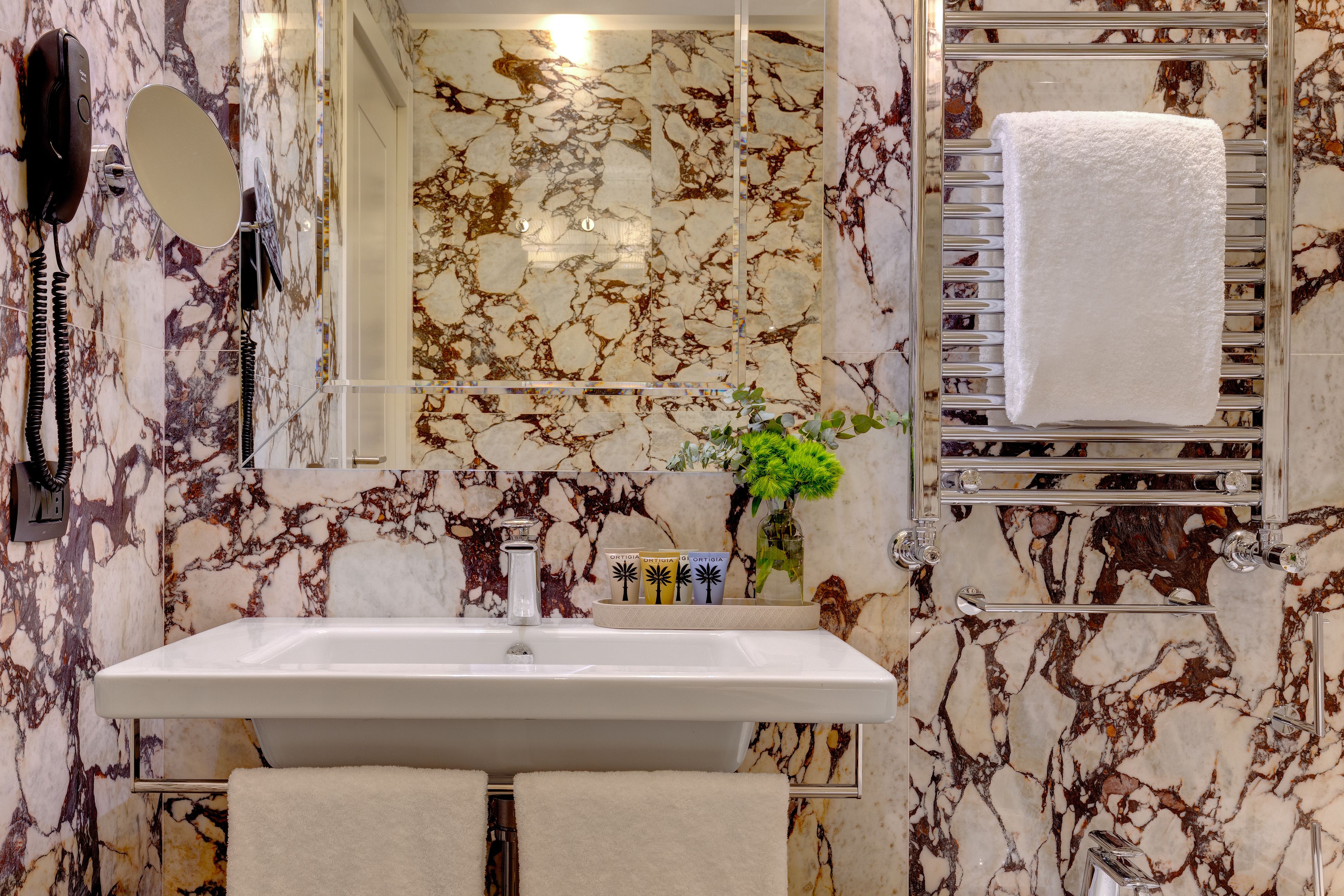 Un bany amb un lavabo de marbre, un mirall, un escurapous i una planta.
